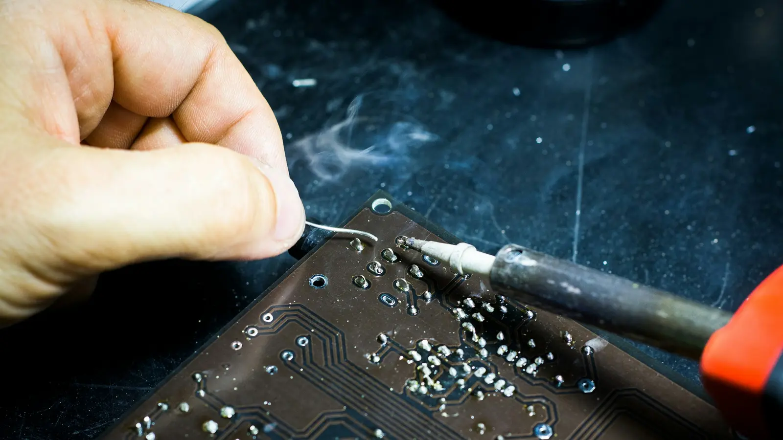 A soldering iron and solder wire working on a circuit board, with flux smoke